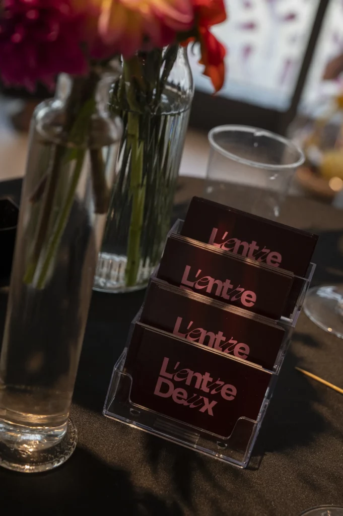 Porte-cartes avec cartes de visite sombres, vase en verre et fleurs floues au premier plan.