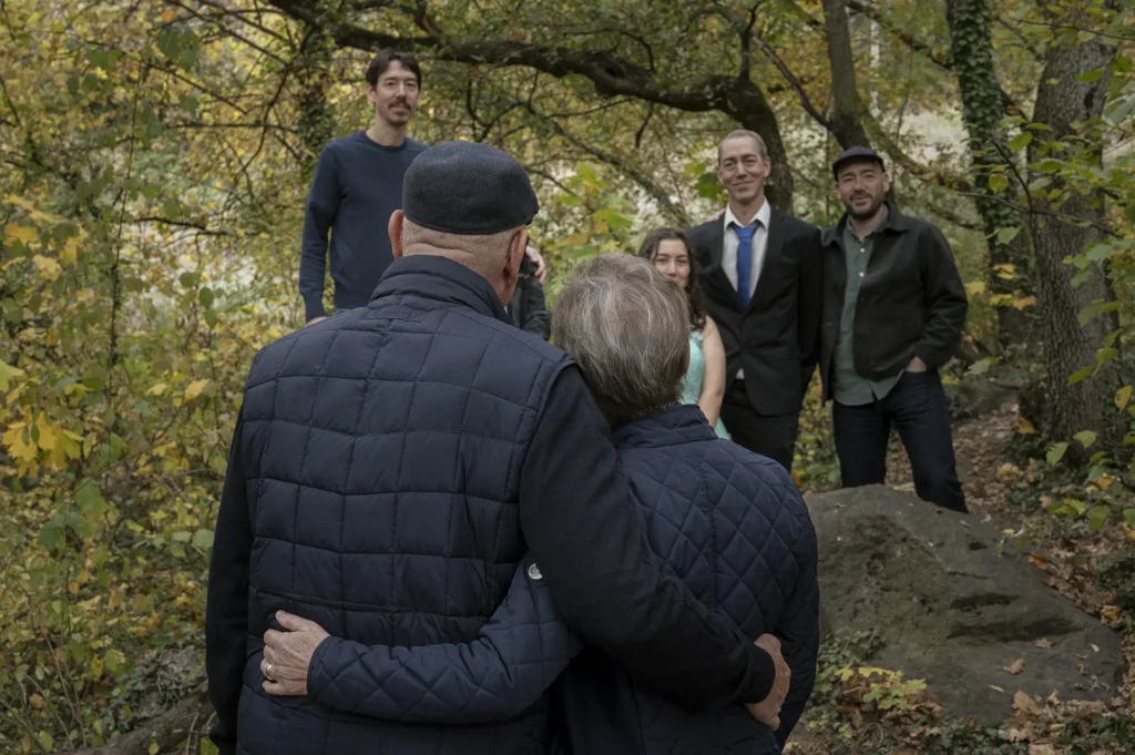 Couple âgé vu de dos, se tenant enlacé dans une forêt d’automne face à un petit groupe de personnes.