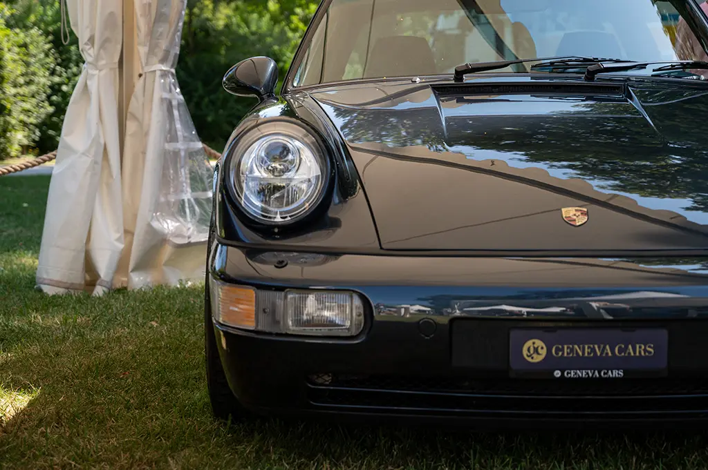 Voiture Porsche noire vue de face, garée sur de l’herbe près d’une tente.