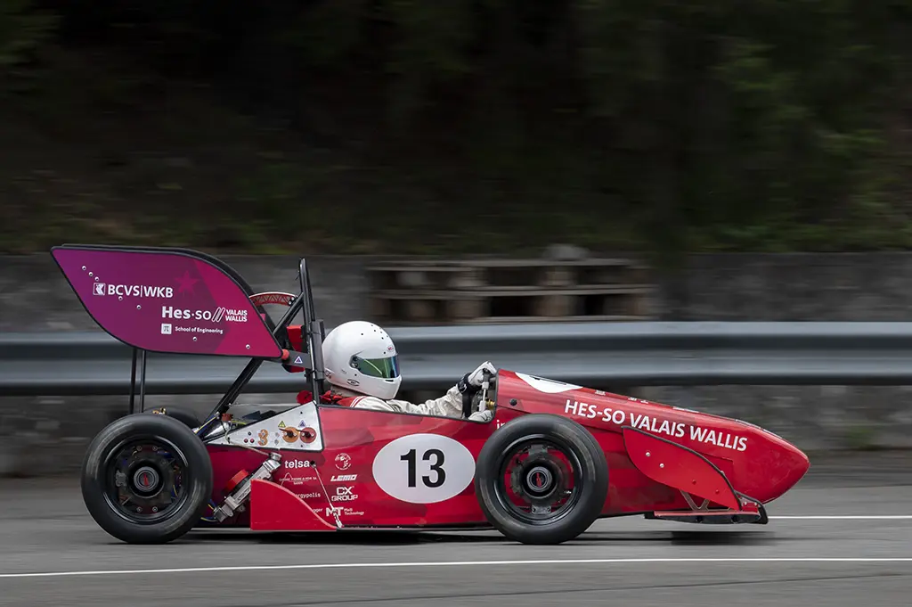 Photo en filé d’un monoplace rouge numéro 13 roulant le long d’une glissière, arrière-plan flou.